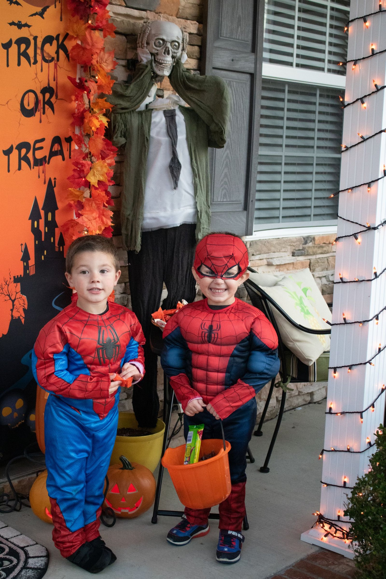 Two kids in superhero costumes enjoying Halloween with decorations and trick-or-treating.